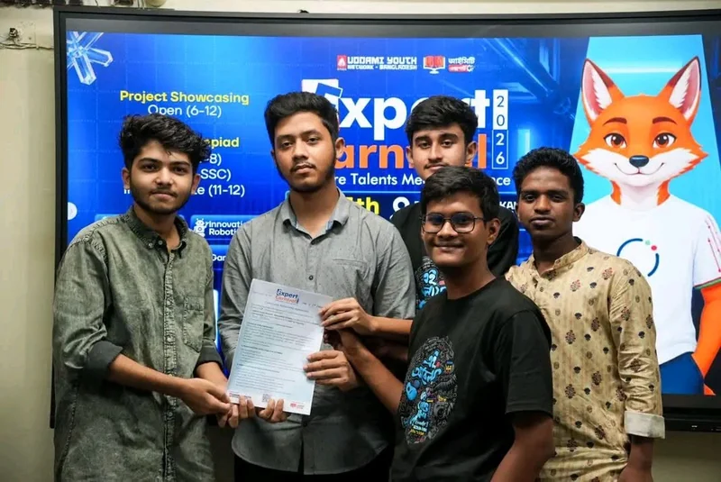 Young men hold a certificate in front of a blue Expert Carnival 2026 backdrop with a fox mascot.