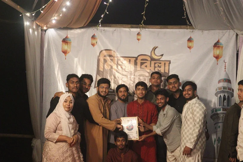 Representatives of youth organisations hold up a certificate of appreciation in front of the Milla Jhilla Cumillar Iftar backdrop.