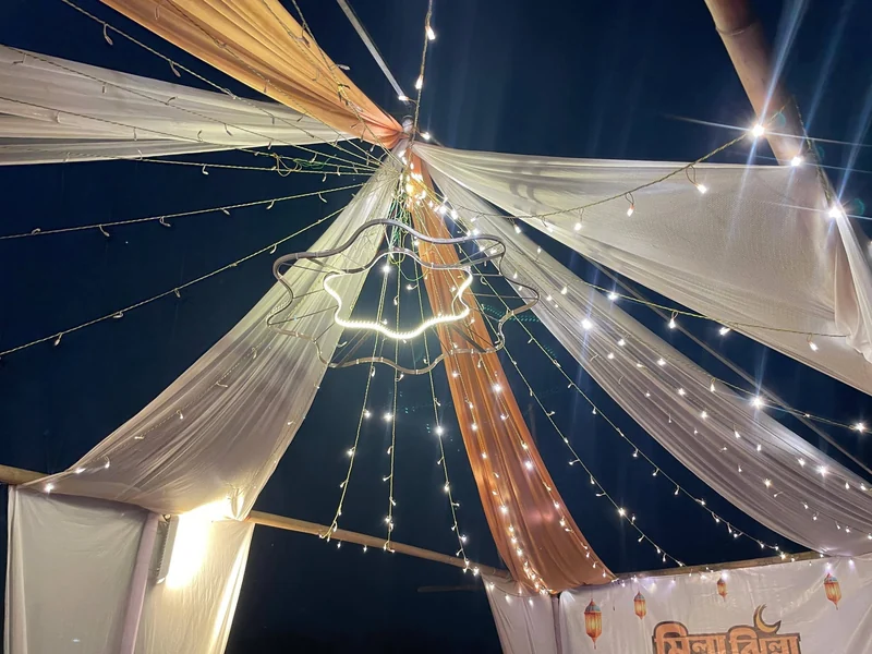 Looking up into a white and peach fabric canopy strung with glowing fairy lights against a deep blue night sky.