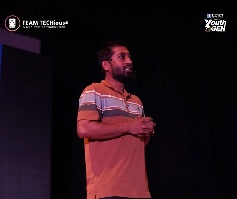 Nahid Rana, in a striped polo shirt, stands on the YouthGEN 2025 stage with his hands clasped.