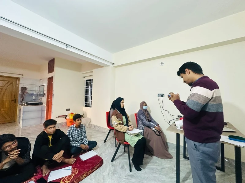 Learners sit on the floor and on chairs taking notes while the trainer operates a projector during a SkillHub design class.