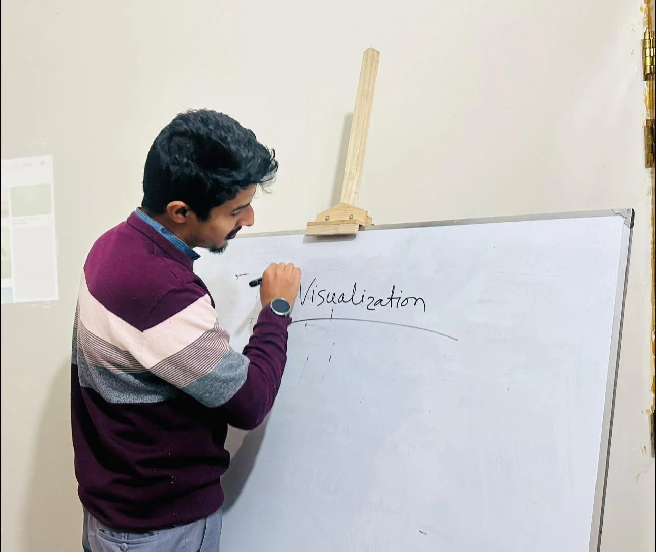 A trainer in a striped sweater writes the word Visualization on a whiteboard during a TECHious SkillHub design session.