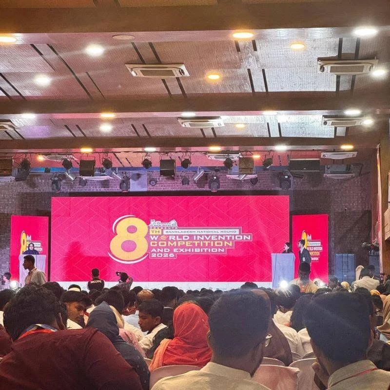 A packed auditorium faces a bright pink stage with the 8th World Invention Competition and Exhibition 2026 banner at Northern University Bangladesh.