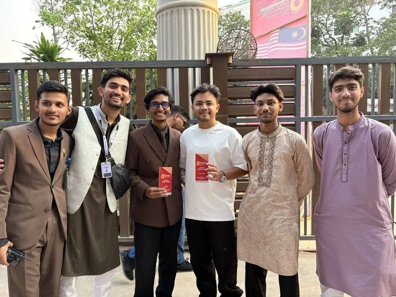 Six young men in panjabis and lanyards stand together outside the Northern University Bangladesh venue on WICE 2026 day.